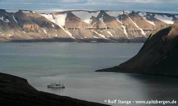 ... contrasting to horizontal layers of younger carbonate rocks further east. Dolerite sill half-way up the slope (seen from Faksevågen across Lomfjord)